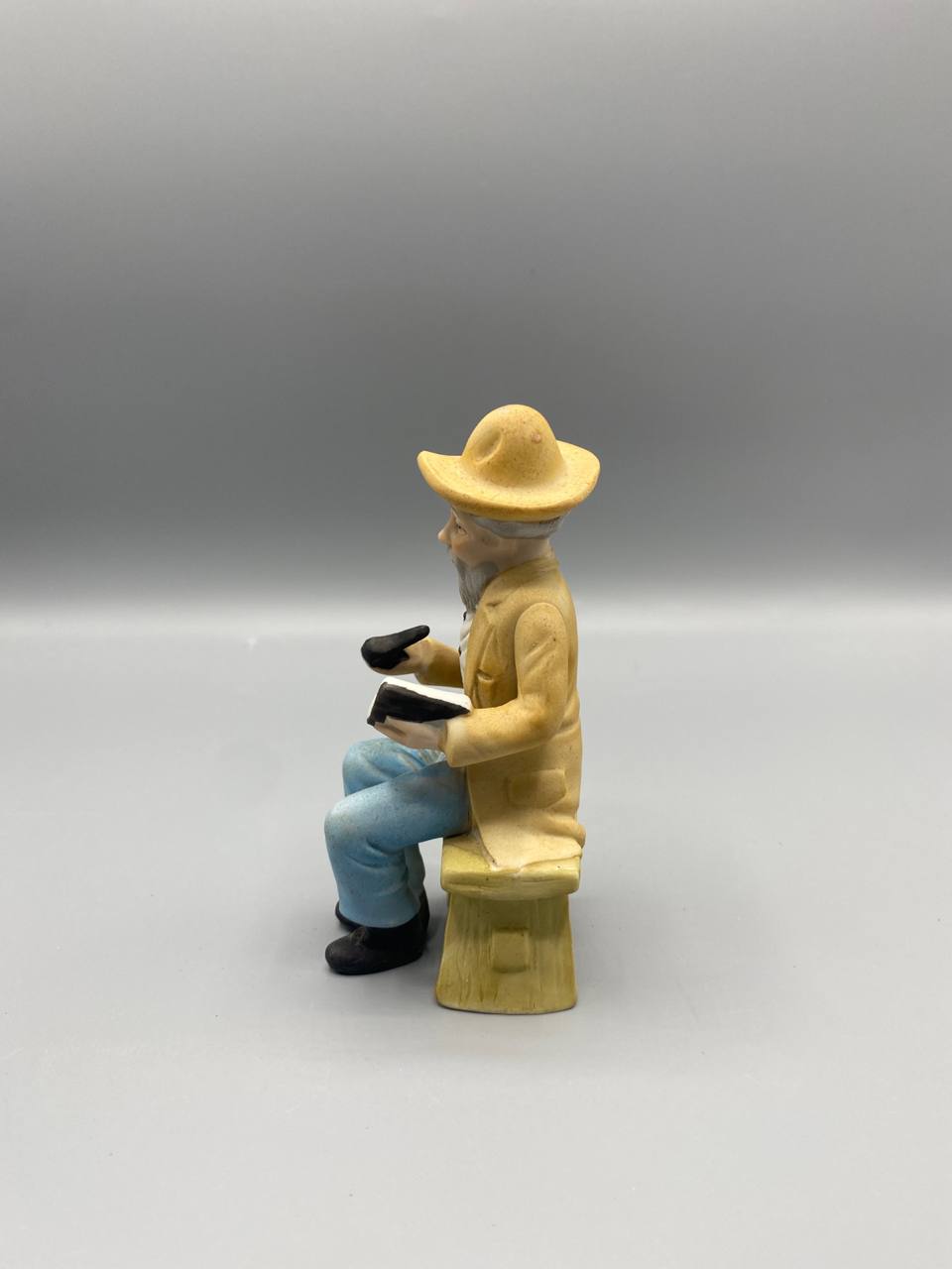 Vue de profil figurine biscuit vieil homme assis pipe livre chapeau paille