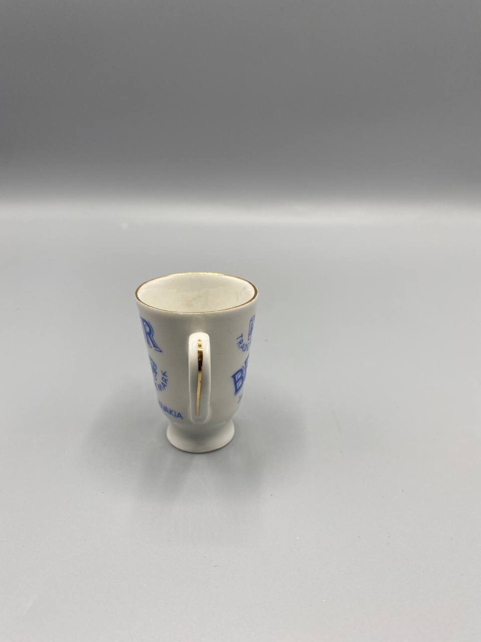 Vue de trois quarts tasse Becherovka anse dorée piédouche porcelaine blanche