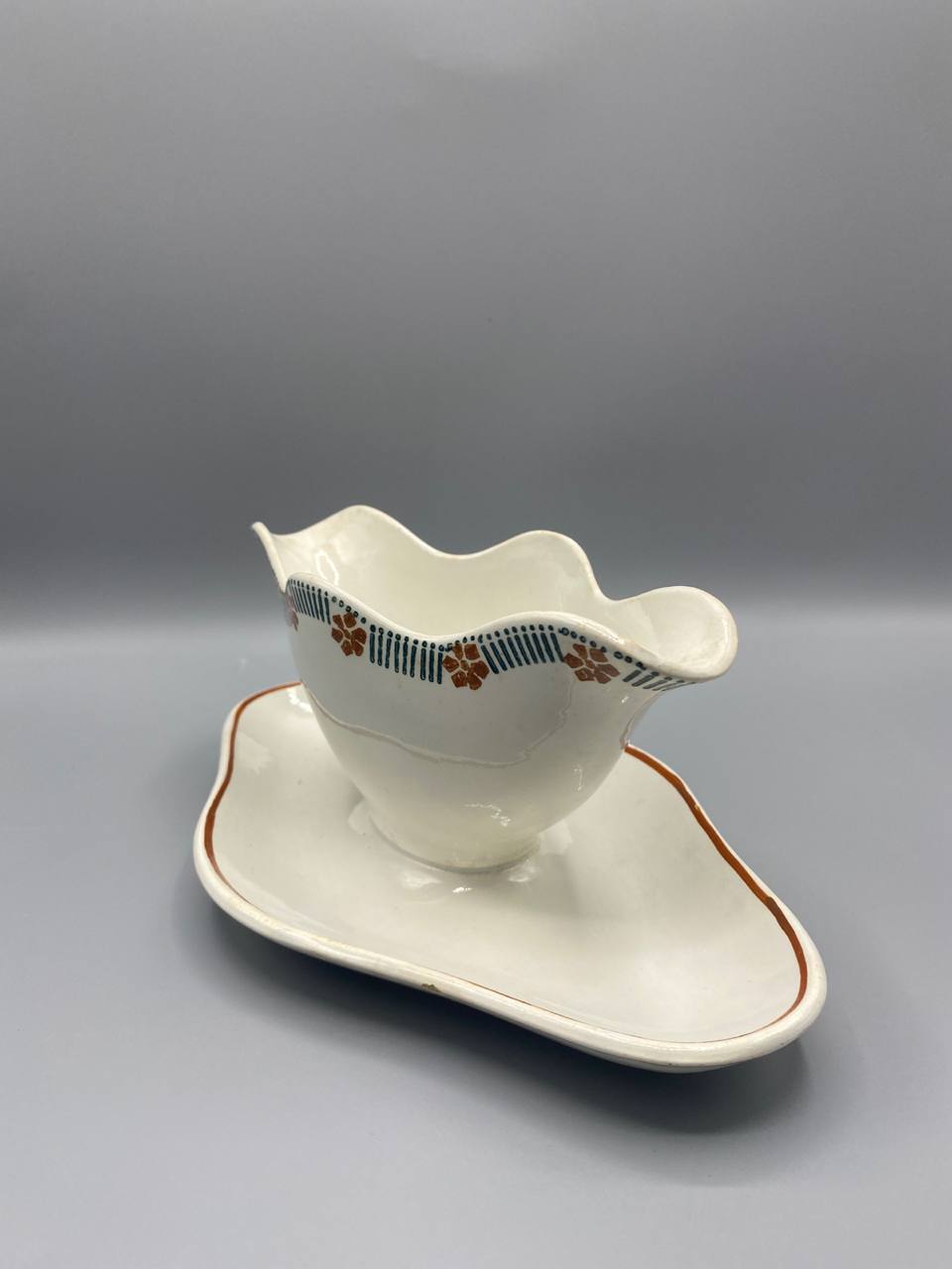 Vue de trois quarts saucière faïence fine Ceranord décor Saraband fleurs brun-rouille bandes bleu-vert