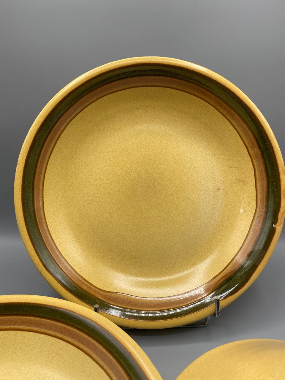 Gros plan assiette plate grès vintage fond beige liseré brun vert olive bord relevé