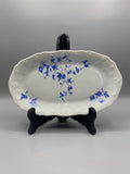 Plat ovale porcelaine blanche décor rosiers bleu cobalt bord festonné relief vue de face sur présentoir