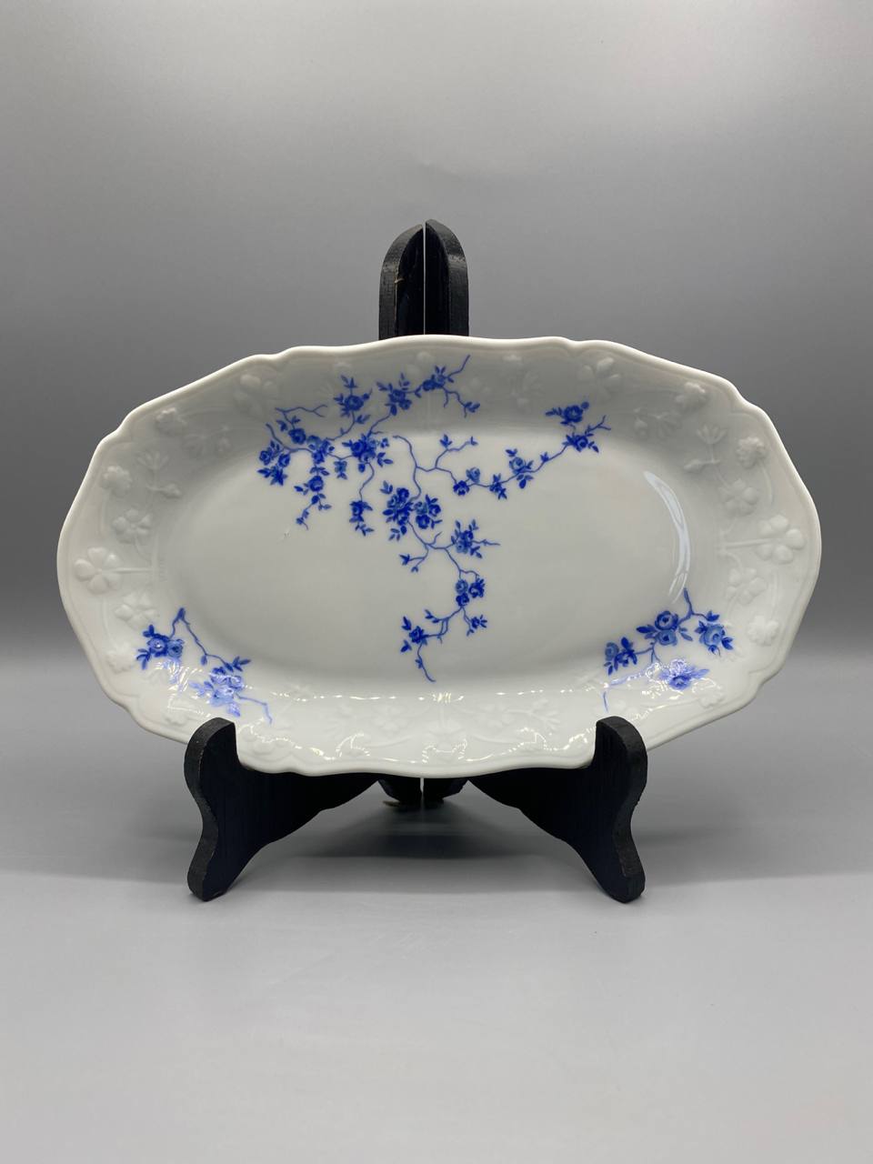 Plat ovale porcelaine blanche décor rosiers bleu cobalt bord festonné relief vue de face sur présentoir