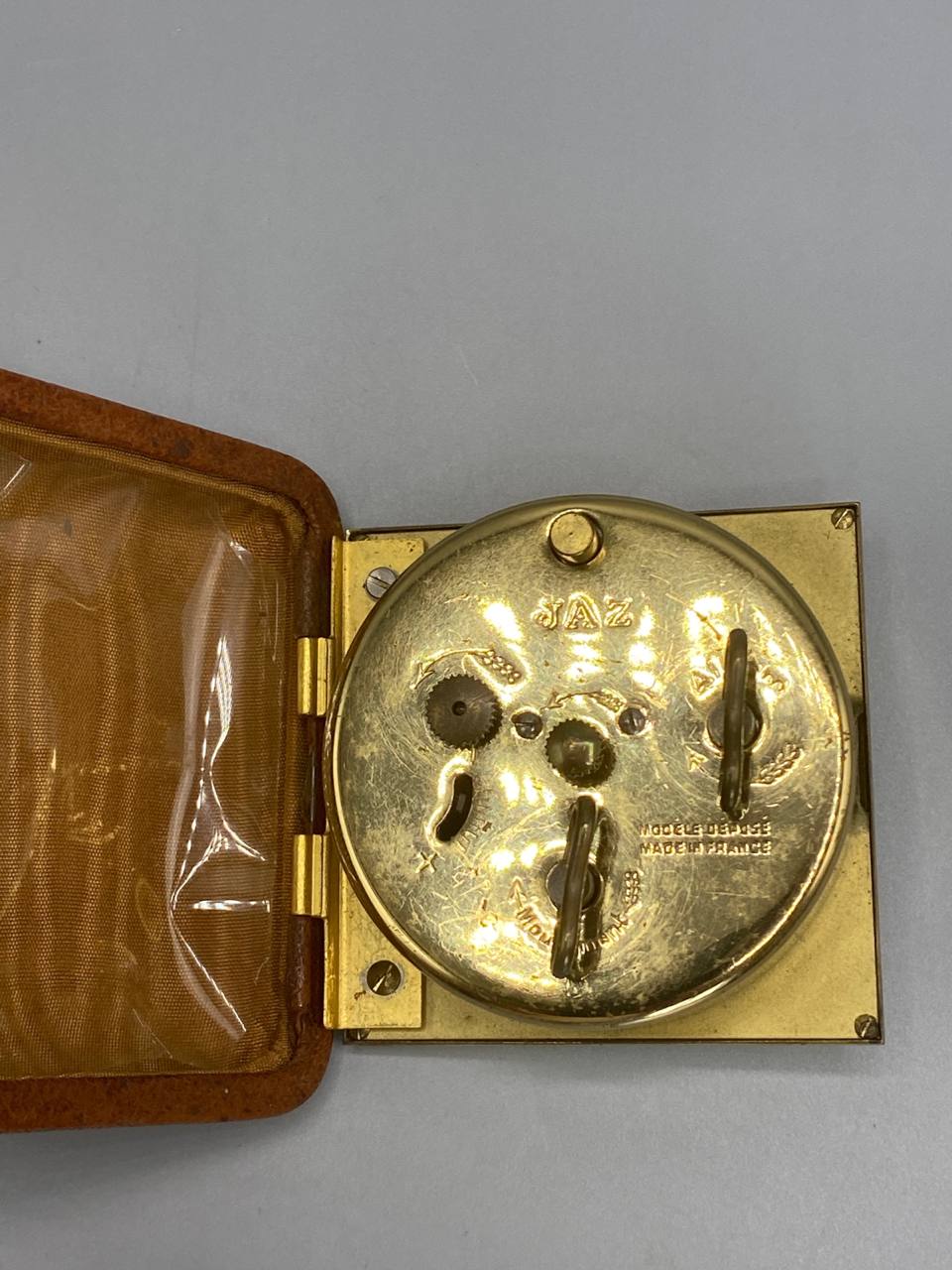 Pendulette de voyage JAZ, dos du mouvement mécanique doré modèle déposé, étui cuir camel ouvert
