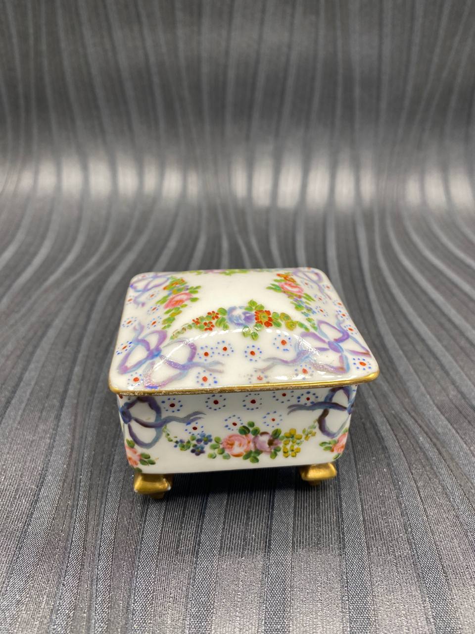 Boîte à bijoux porcelaine blanche, vue de face, guirlandes florales et rubans mauves peints à la main, pieds dorés