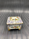 Boîte à bijoux porcelaine blanche, vue de face, guirlandes florales et rubans mauves peints à la main, pieds dorés