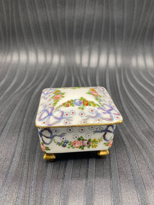 Boîte à bijoux porcelaine blanche, vue de face, guirlandes florales et rubans mauves peints à la main, pieds dorés