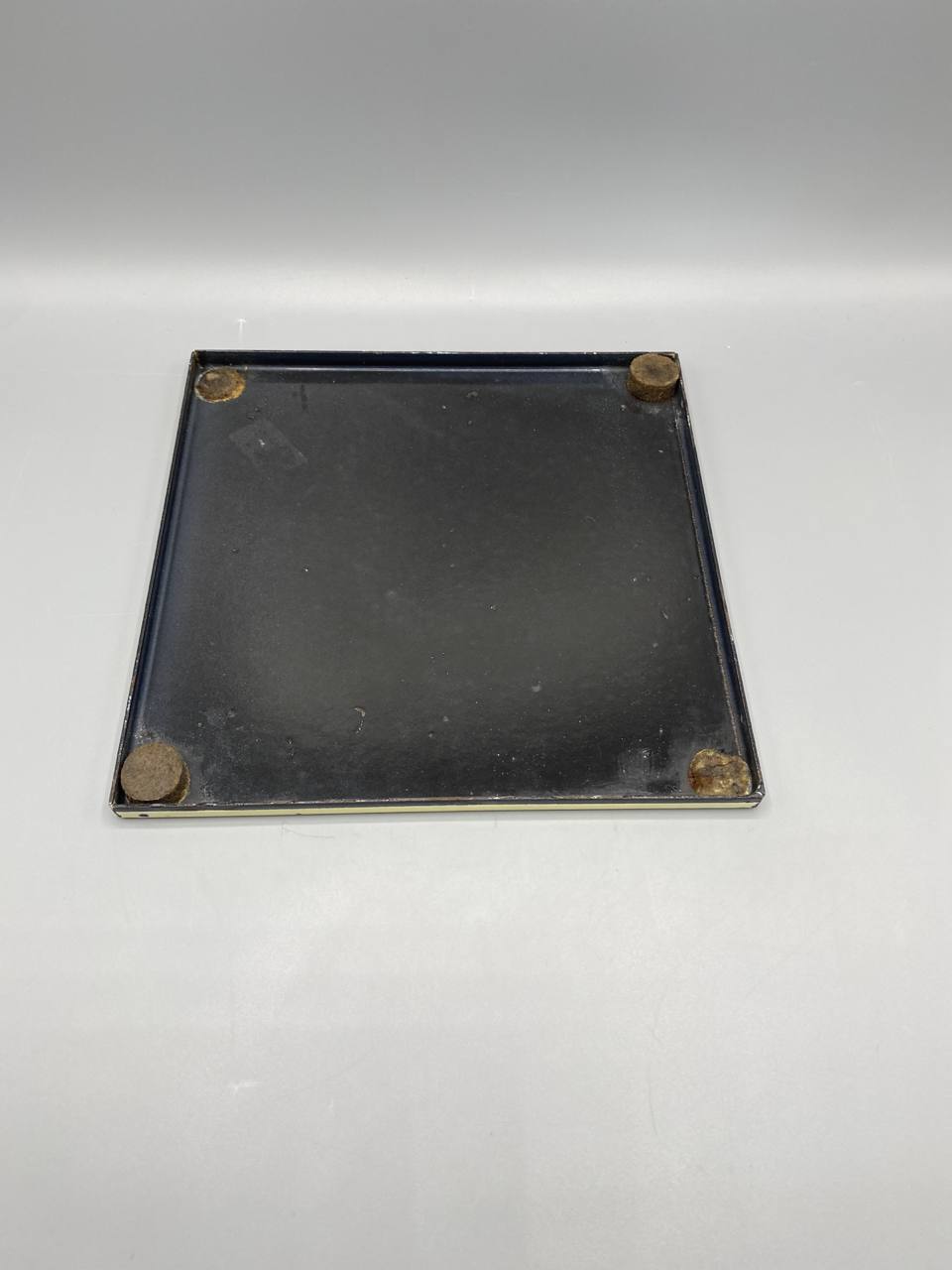 Dos du dessous-de-plat, métal laqué noir, 4 pieds caoutchouc d'origine aux coins