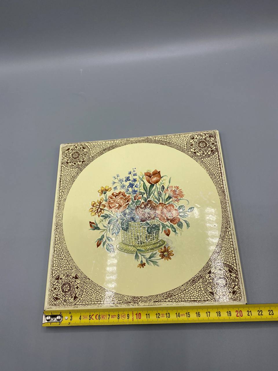 Dessous-de-plat émail sur métal avec mètre ruban, environ 20 cm de côté, vue de face