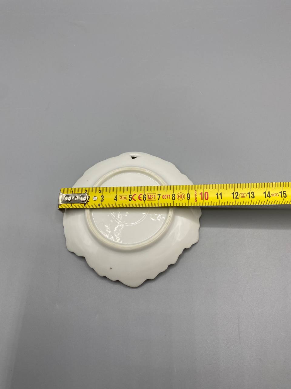 Dos de la coupelle, fond blanc, pied annulaire, mètre ruban diamètre environ 13 cm