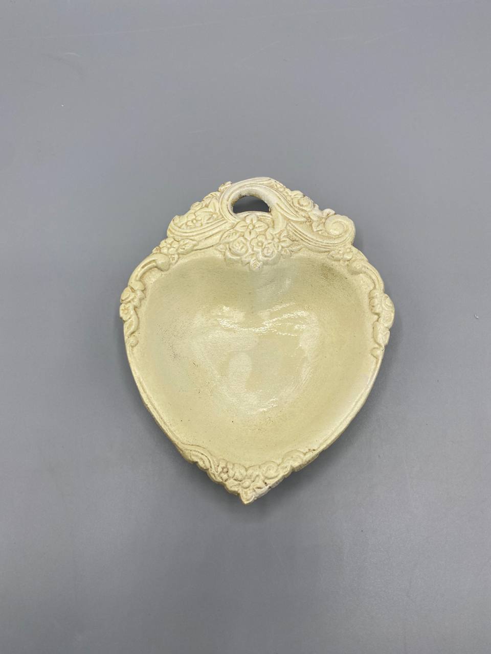 Coupelle céramique ivoire en forme de coeur, vue de face, décor rocaille fleurs et volutes en relief, anneau de suspension