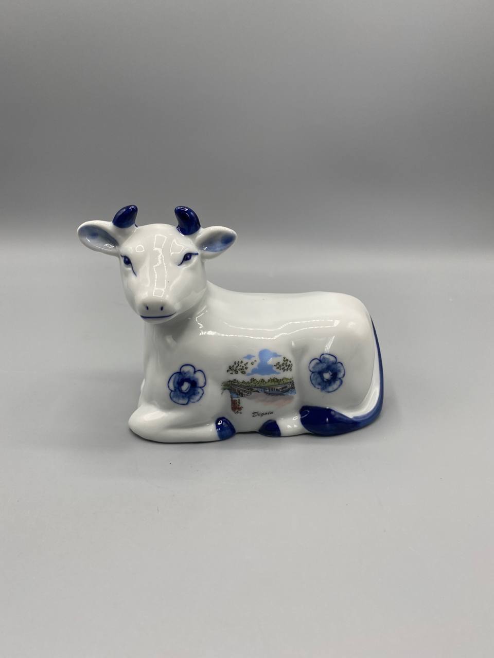 Figurine vache couchée faïence blanche et bleue, vue de face, vignette pont-canal Digoin, fleurs bleues, cornes émaillées bleu