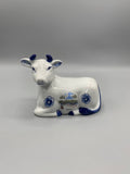 Figurine vache couchée faïence blanche et bleue, vue de face, vignette pont-canal Digoin, fleurs bleues, cornes émaillées bleu