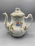 Cafetière ancienne porcelaine blanche, vue de face, décor marguerites bleues et roses, liseré doré, couvercle à prise feuillagée