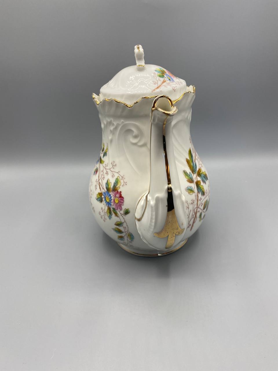 Cafetière, vue de trois quarts côté anse, motifs en relief sur l'épaule, couvercle à prise noeud feuillagé