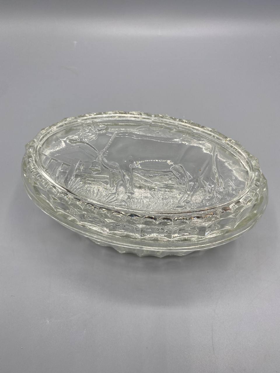 Beurrier verre pressé transparent, vue de trois quarts, couvercle à cloche avec vache au pré en relief, plateau ovale godronné