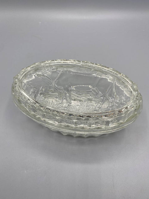 Beurrier verre pressé transparent, vue de trois quarts, couvercle à cloche avec vache au pré en relief, plateau ovale godronné