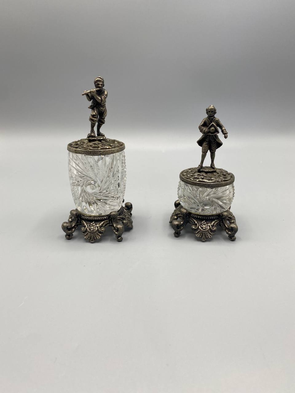 Paire de moutardiers Belle Époque, vue de face, cristal taillé sur socle métal argenté, couvercles figurines joueur de flûte et gentilhomme XVIIIe