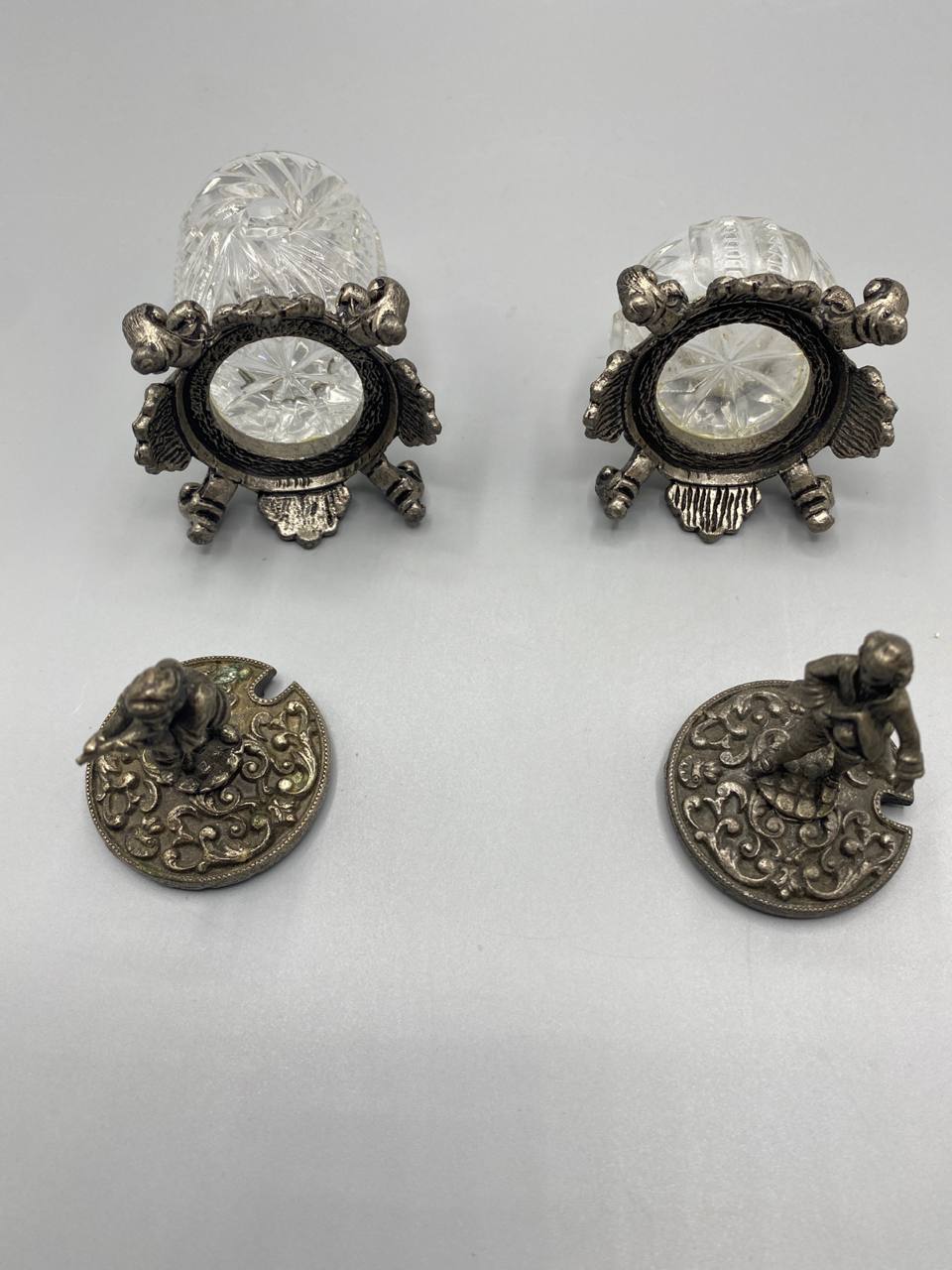 Couvercles métal argenté vus de dessous, décor rinceaux et volutes ajournés, encoche pour cuillère visible, figurines putti allongés
