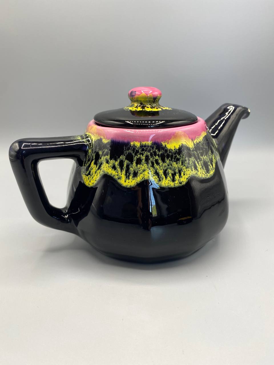 Théière Vallauris, vue de face, panse octogonale noire avec coulées rose fuchsia et jaune chartreuse, bouton couvercle rose
