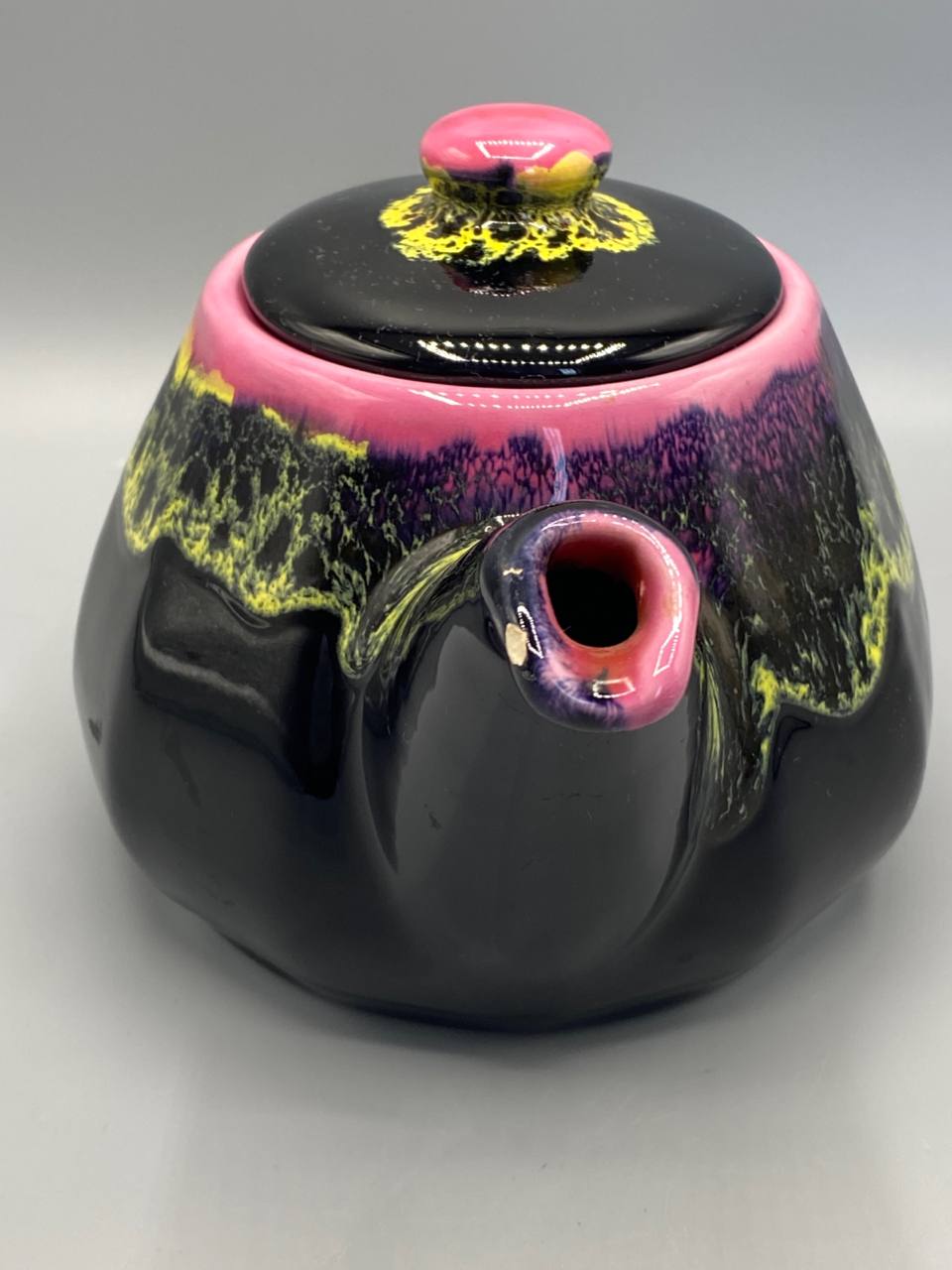 Théière Vallauris, vue de profil côté bec verseur, silhouette globulaire, émail noir brillant, coulées violettes et jaunes visibles
