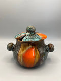 Pot à couvercle Vallauris, vue de face, panse globulaire brun chocolat avec coulées orange vif, couvercle turquoise craquellé à bouton rond