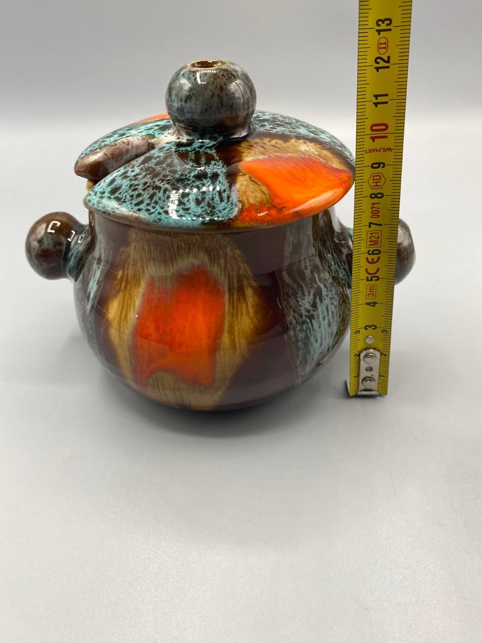 Pot Vallauris fermé avec mètre ruban, hauteur totale avec couvercle environ 11 cm, vue de profil, coulées orange et turquoise visibles