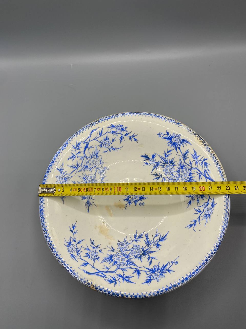 Compotier vu de profil avec mètre ruban, hauteur environ 8 cm, piédouche et bord à frise perlée bleue visibles
