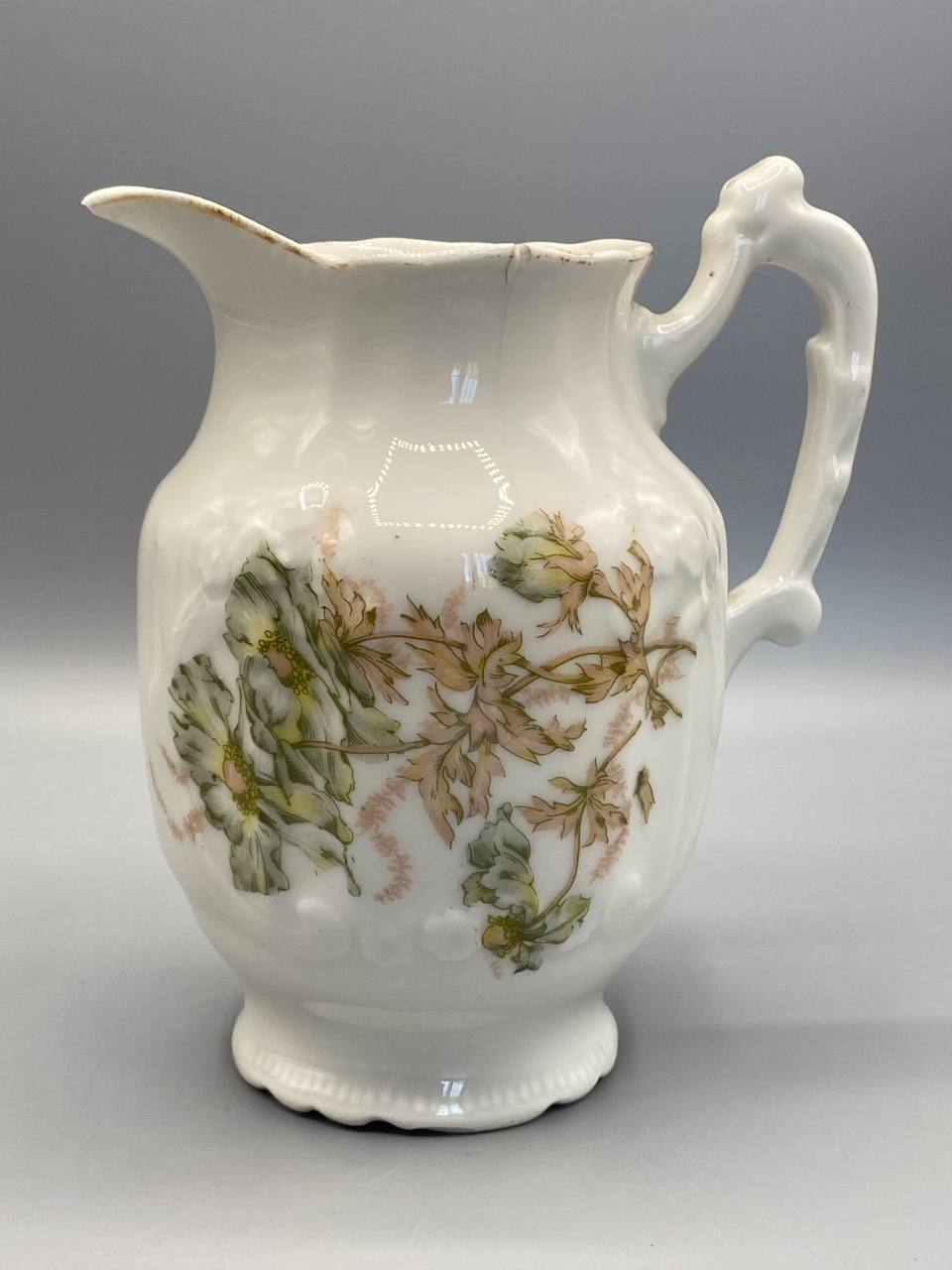Pot à lait porcelaine blanche, face principale, décor floral polychrome vert tendre et rose poudré, frise de grappes en relief sur la panse, anse sculptée