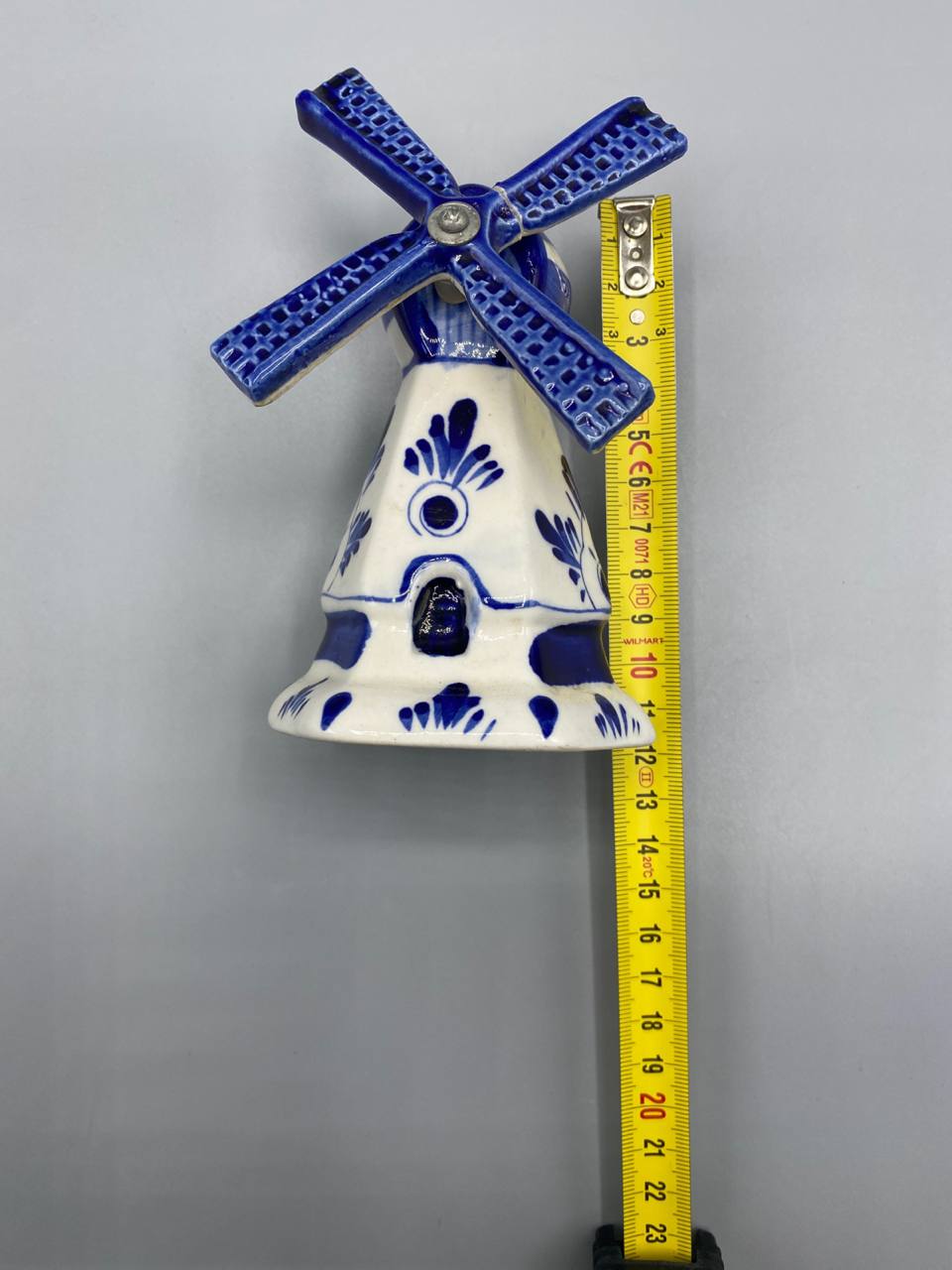Moulin hollandais Delft bleu avec mètre ruban, hauteur environ 12 cm, vue de face, ailes mobiles en croix, décor floral bleu cobalt sur fond blanc