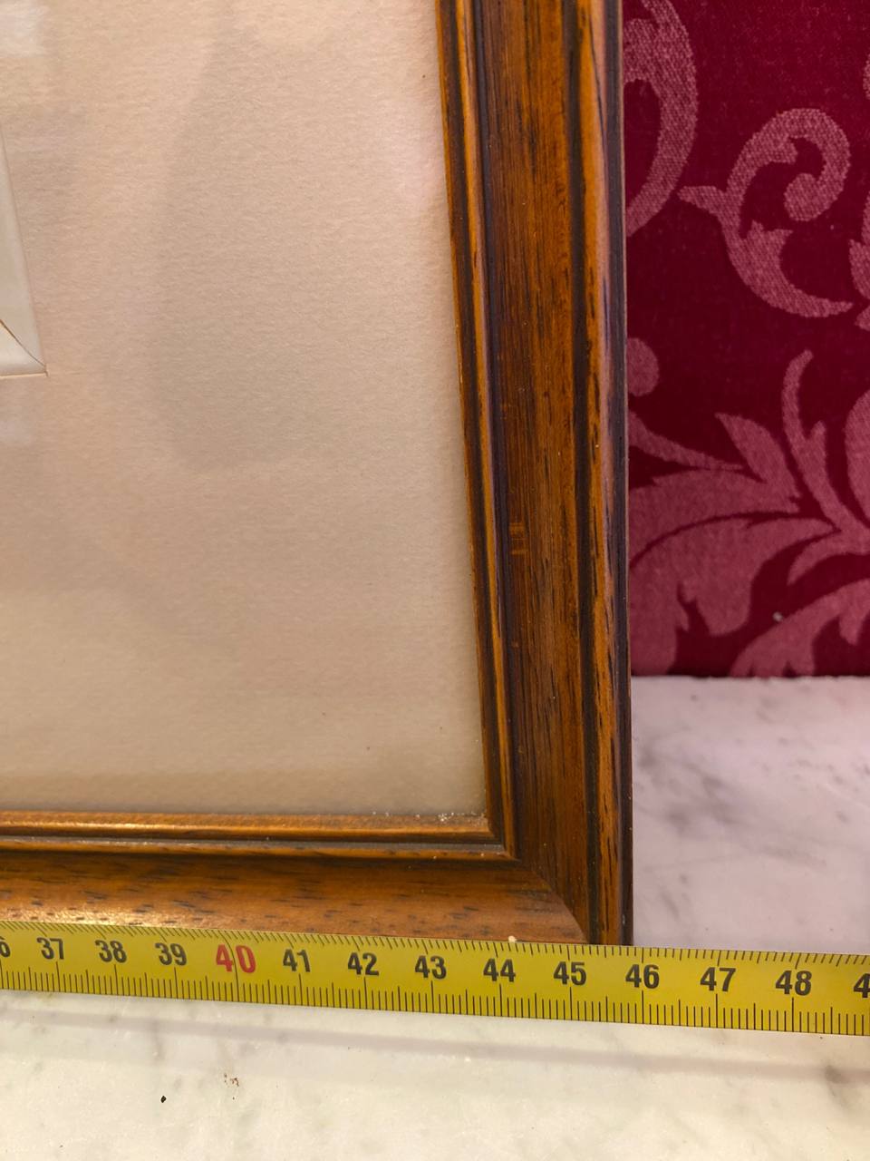 Mesure de la hauteur du cadre avec mètre ruban, environ 45 cm, angle inférieur du cadre bois patiné, passe-partout crème visible