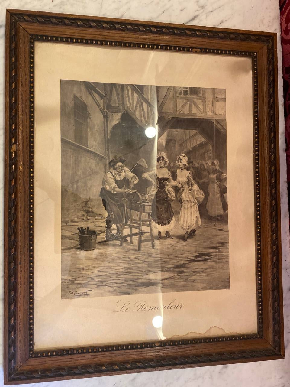 Gravure ancienne Le Remouleur signée F.R. Duport, vue d'ensemble encadrée, cadre chêne sculpté à perles dorées, passe-partout crème, scène de rue Belle Époque