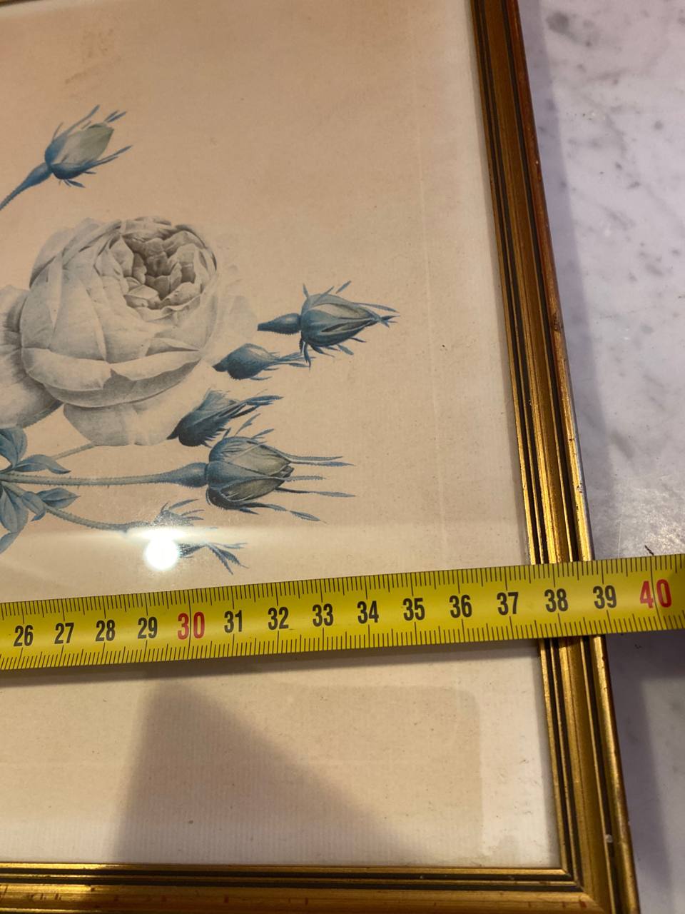 Mesure de la largeur du cadre avec mètre ruban, environ 40 cm, angle supérieur droit du cadre doré cannelé, boutons de rose bleus visibles