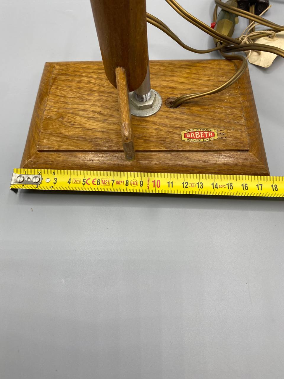 Mesure de la profondeur du socle en bois avec mètre ruban, environ 13-14 cm, bras articulé et tige chromée visibles, étiquette BABETH partiellement visible