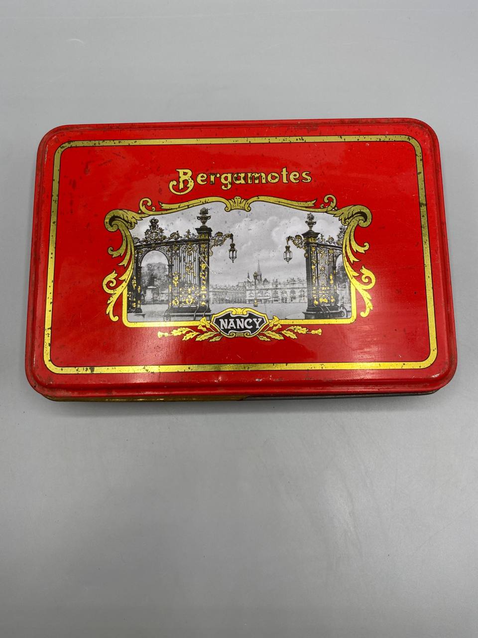 Boîte Bergamotes Nancy – couvercle fermé, médaillon grilles Place Stanislas sur fond rouge
