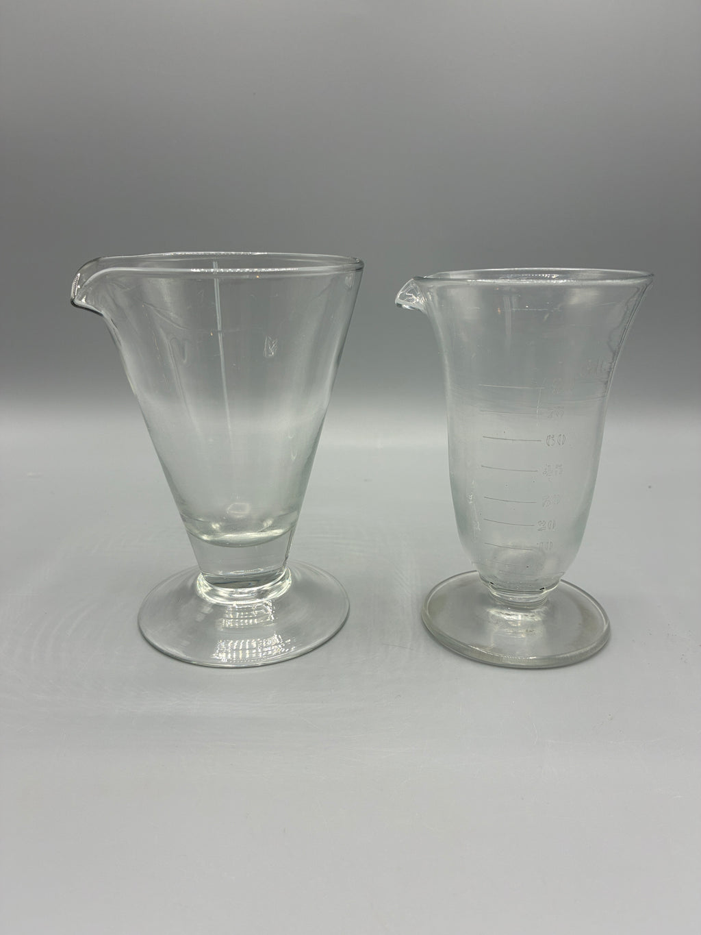 Deux anciens verres doseurs à pied et bec verseur