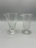 Deux anciens verres doseurs à pied et bec verseur