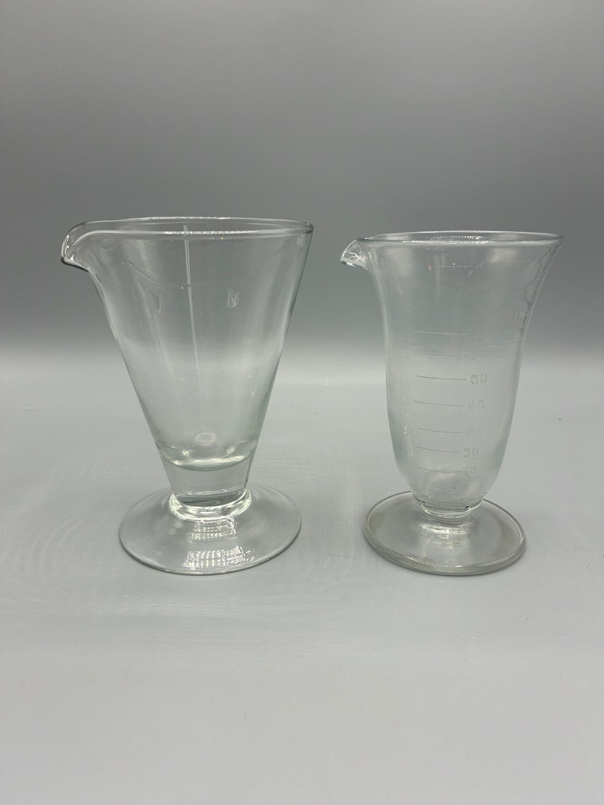 Deux anciens verres doseurs à pied et bec verseur