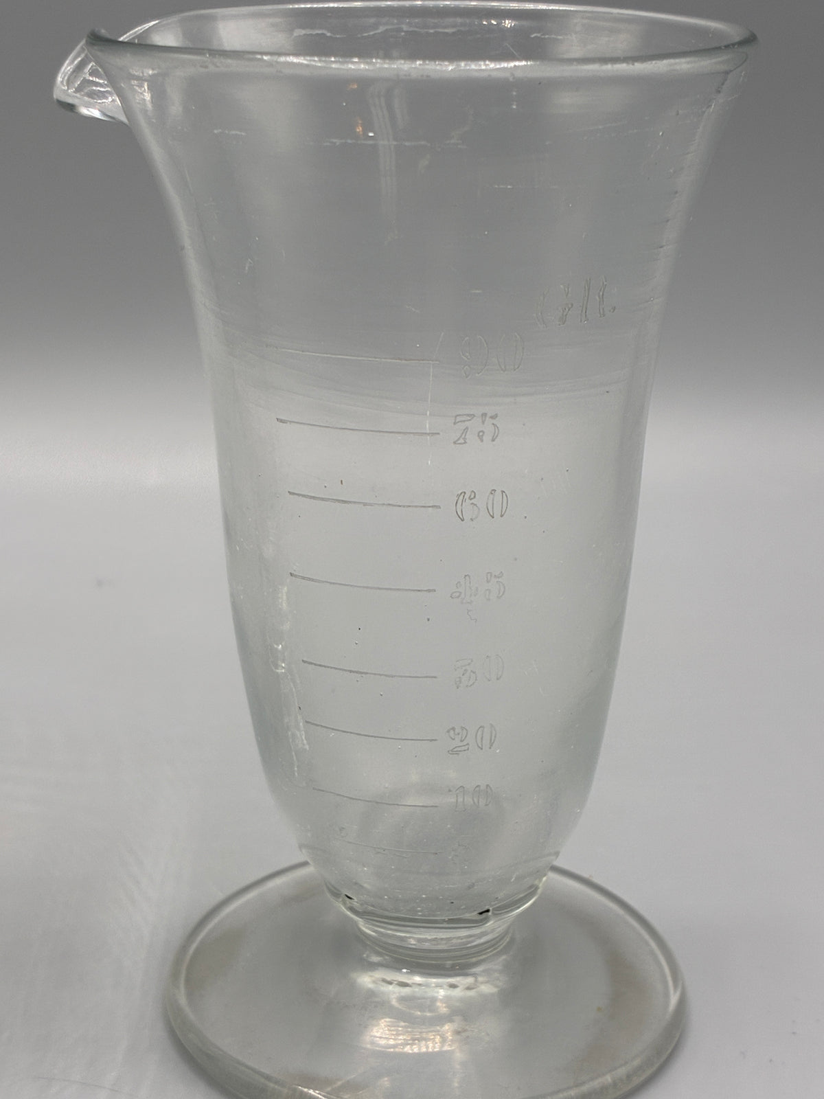 Grand verre doseur ancien à pied circulaire
