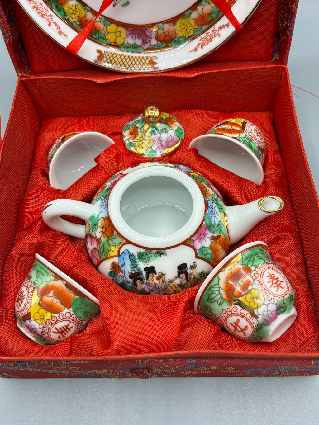 Service à saké en porcelaine polychrome avec verseuse, quatre coupelles et assiette dans son coffret rouge ouvert