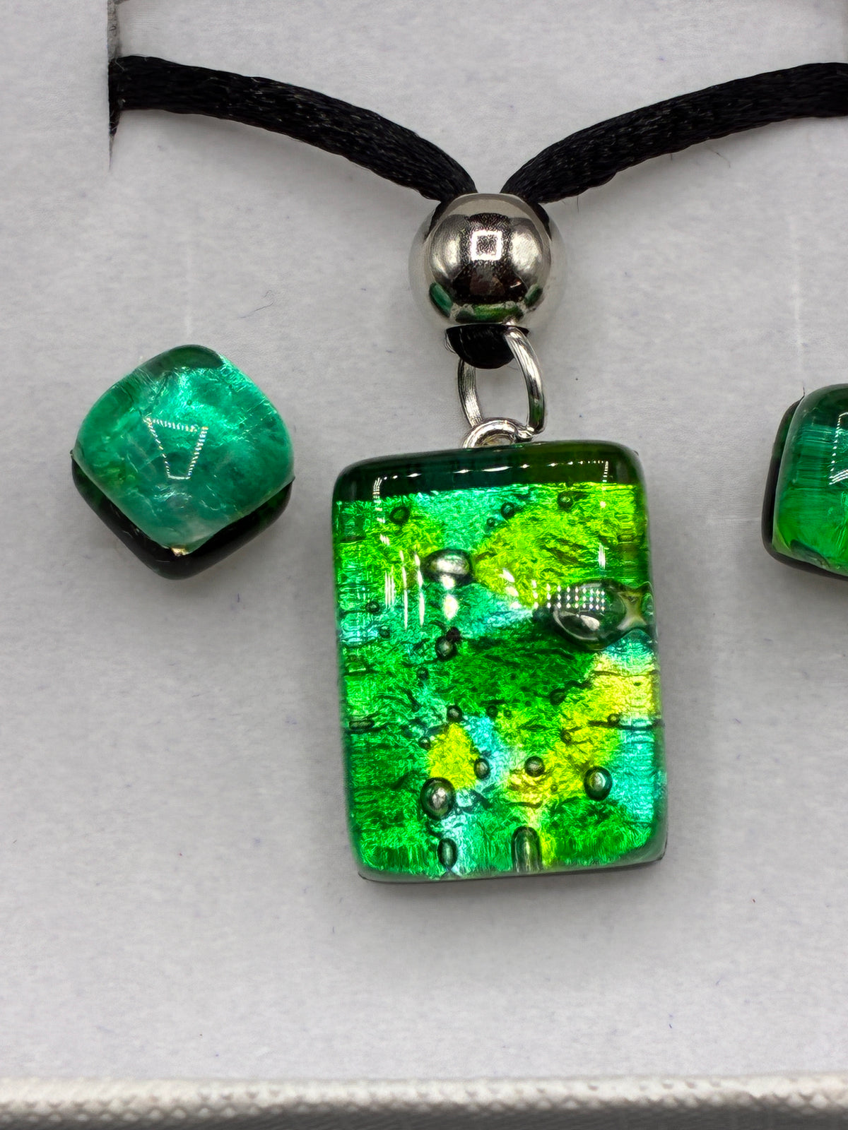 Collier à pendentif vert sur cordon noir présenté sur buste et boucles d’oreilles assorties en écrin