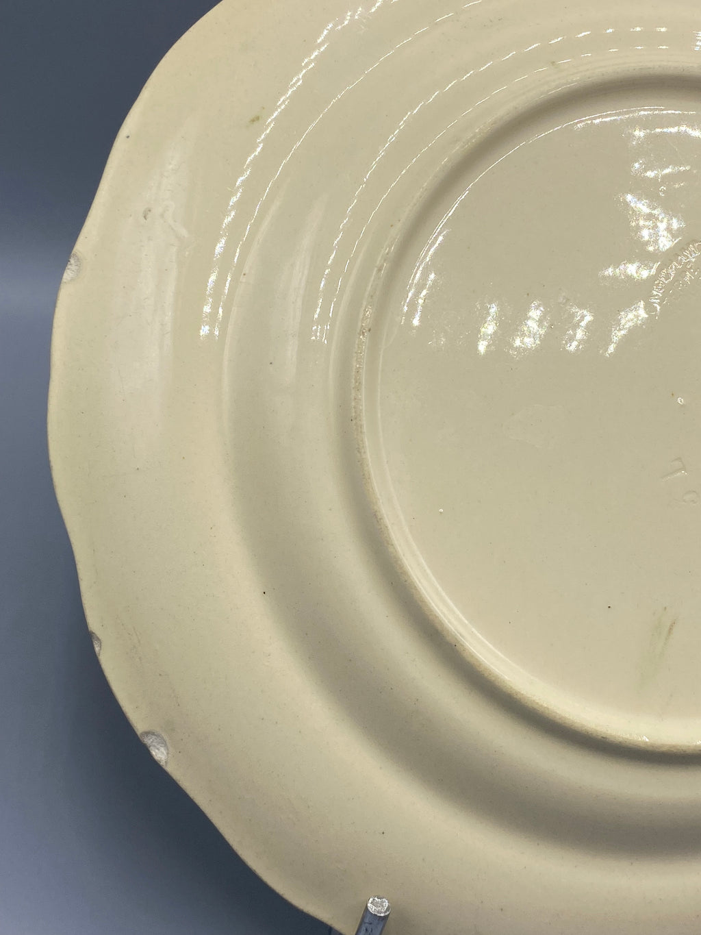 Revers assiette faïence Moustiers, fond crème, éclats et traces d'usage visibles