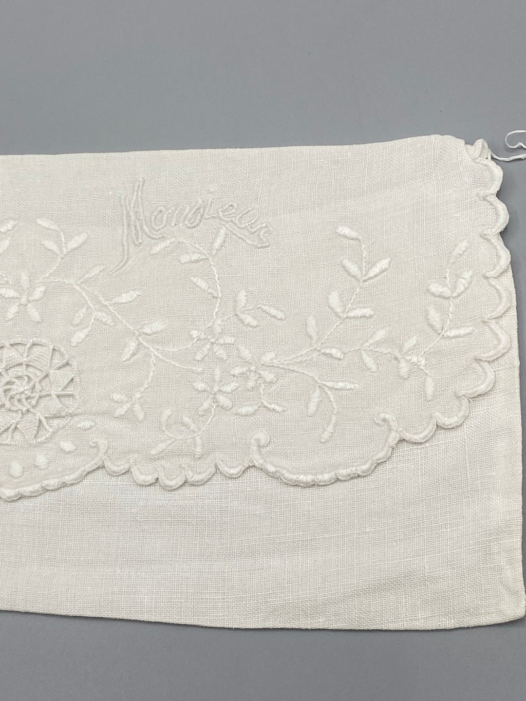 Détail broderie Monsieur en écriture cursive – branches fleuries et médaillon ajouré