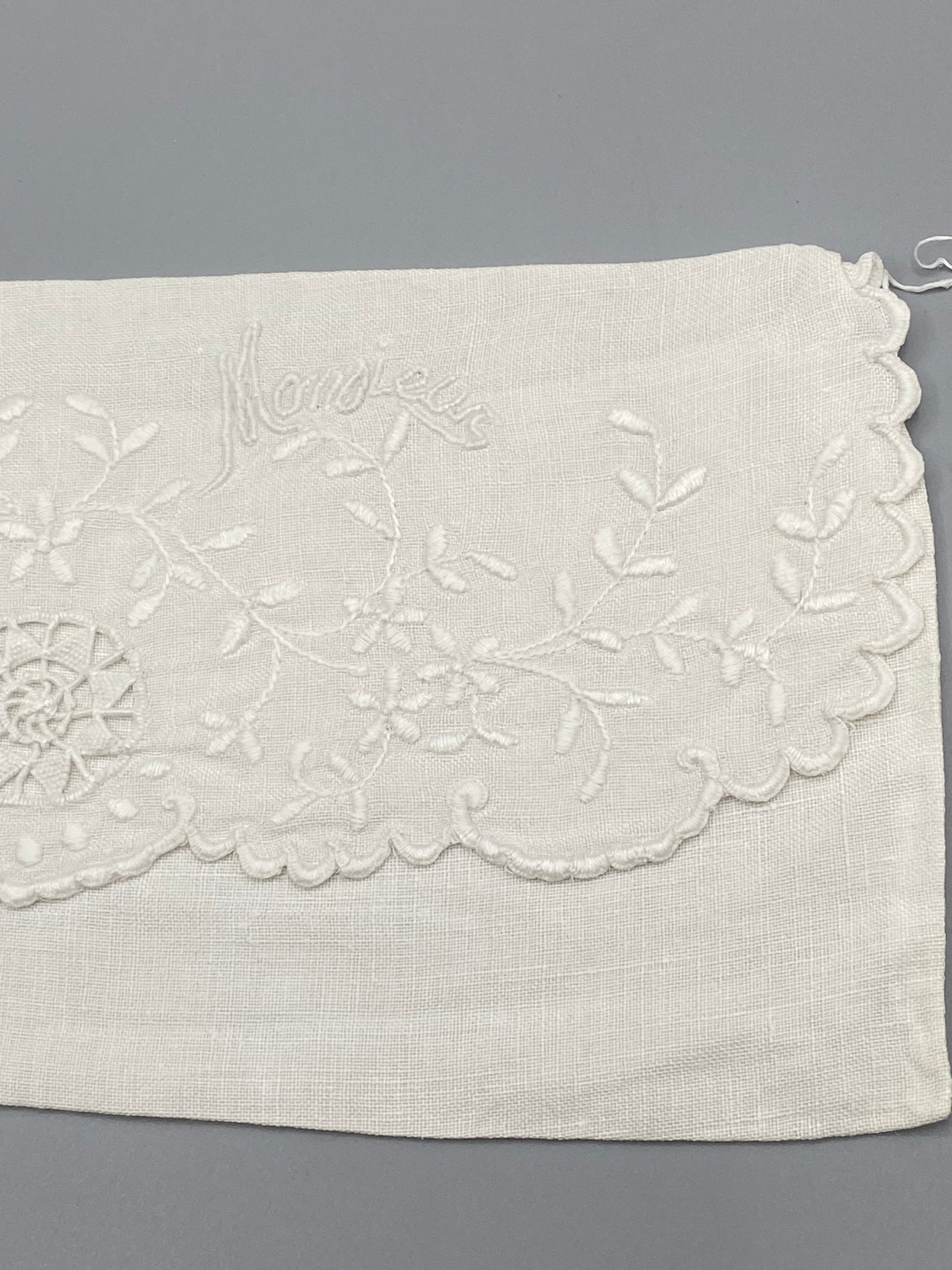 Détail broderie Monsieur en écriture cursive – branches fleuries et médaillon ajouré