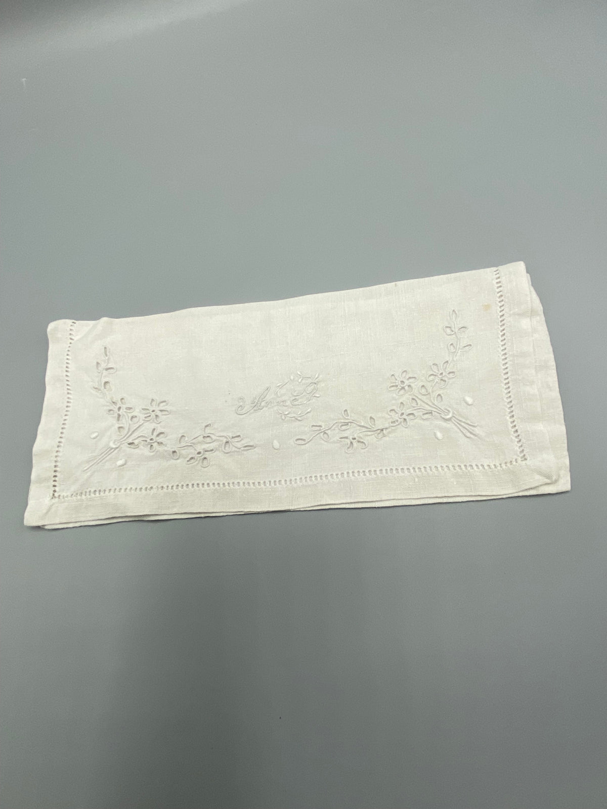 Détail broderie prénom Anne en cursive blanche – motif floral et jours à fils tirés
