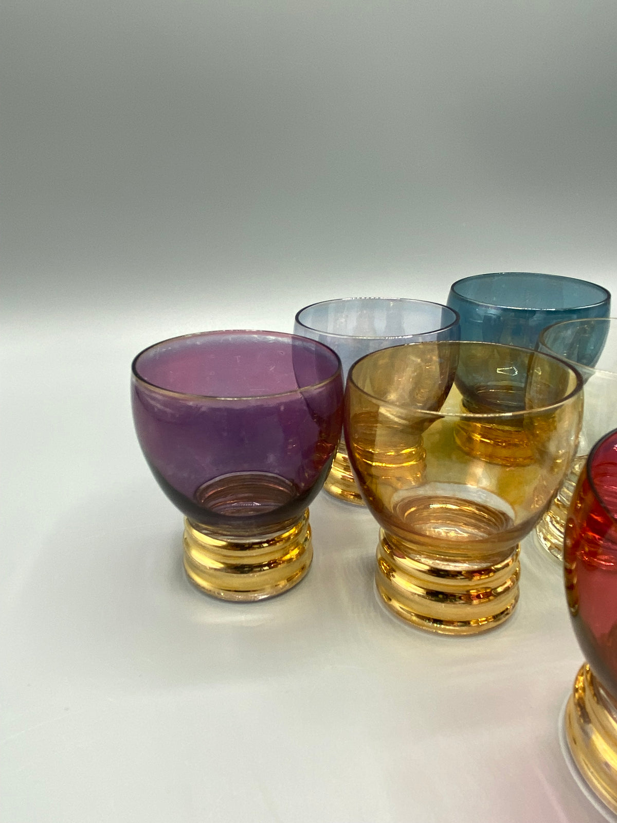 Présentation des sept verres à liqueur aux teintes variées et pieds dorés
