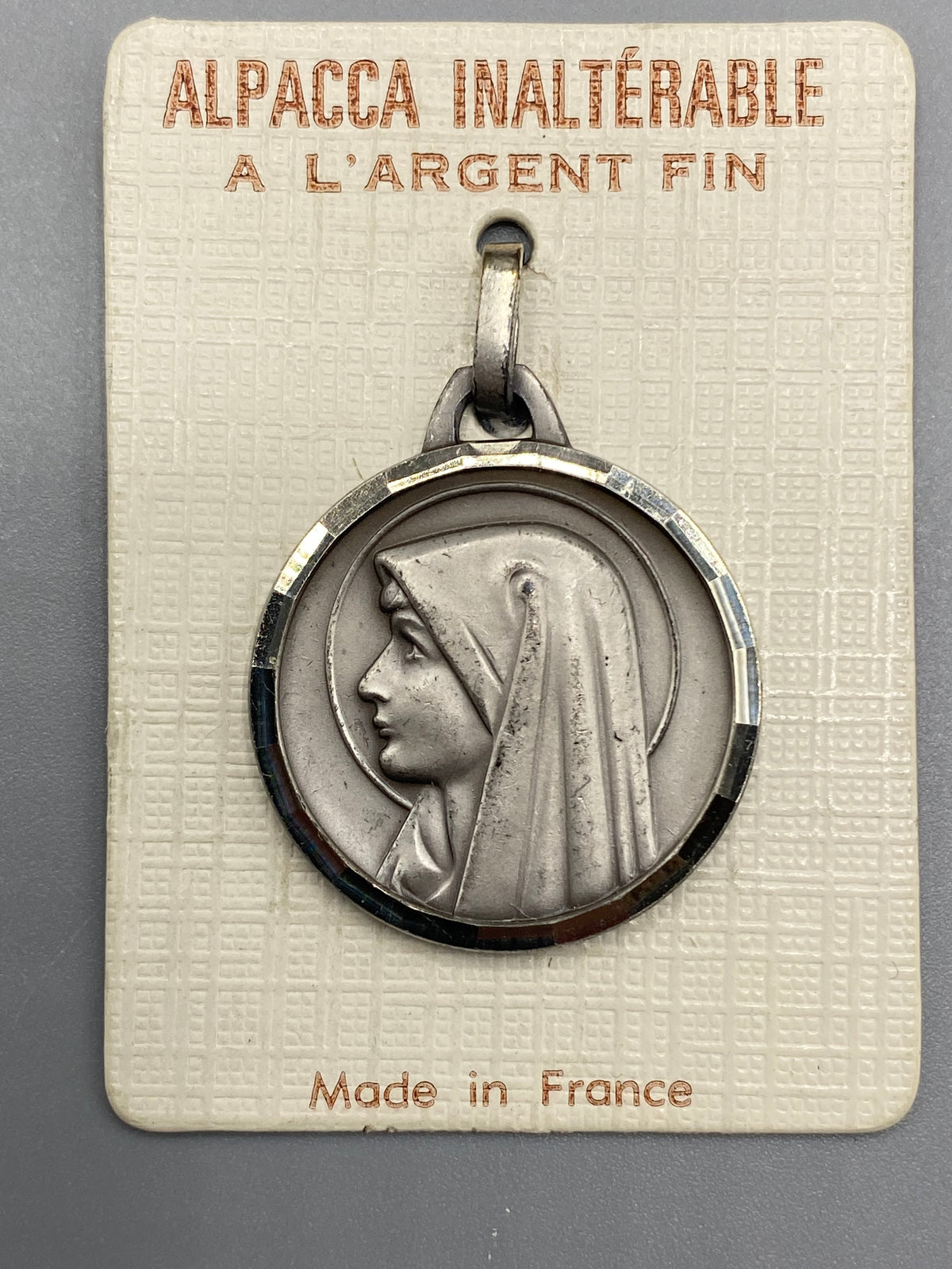 Médaille ancienne de la Vierge Marie de profil en Alpacca argenté sur son cartonnage d’origine