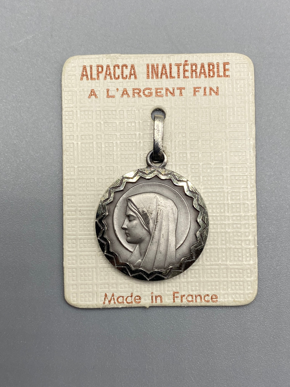 Médaille Vierge Marie en Alpacca argenté à bordure géométrique sur son cartonnage d’origine