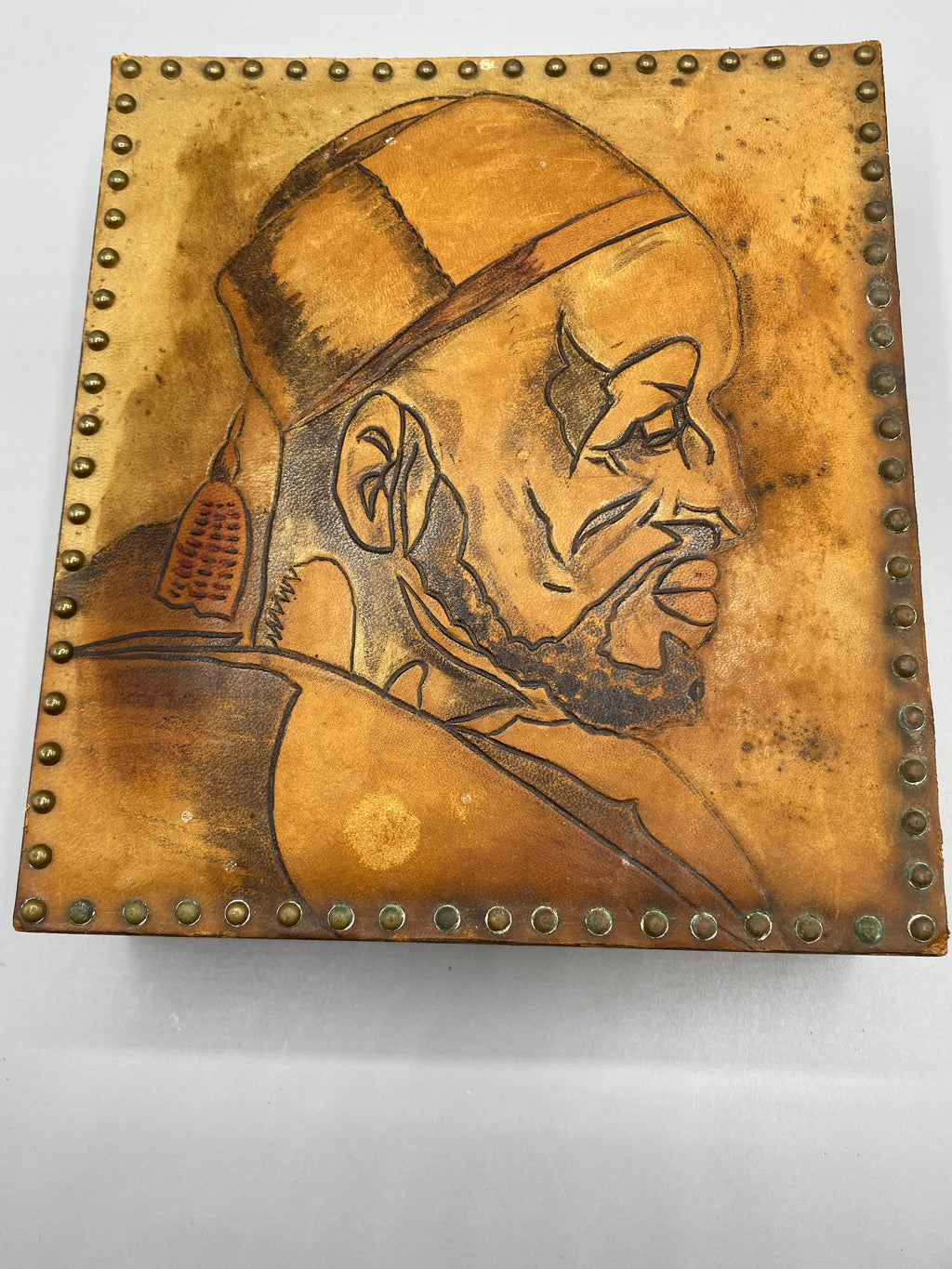 Portrait masculin de profil sur le cuir fauve, bordure de clous métalliques